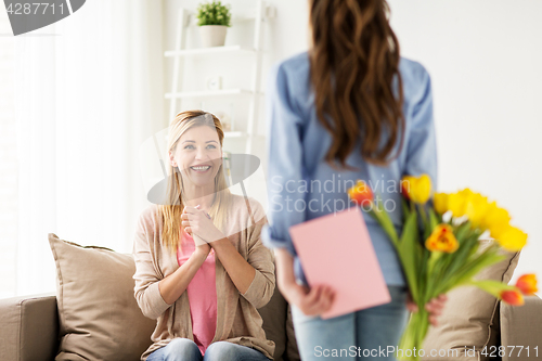 Image of happy girl giving flowers to mother at home