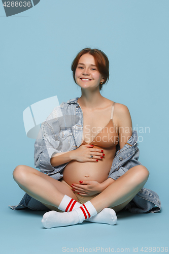 Image of Young beautiful pregnant woman sitting on blue background