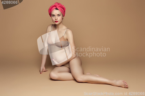 Image of Young beautiful pregnant woman sitting on brown background