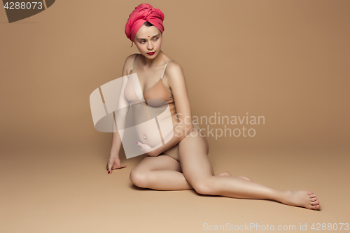 Image of Young beautiful pregnant woman sitting on brown background