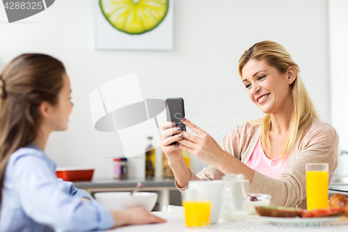 Image of woman photographing daughter by smartphone at home