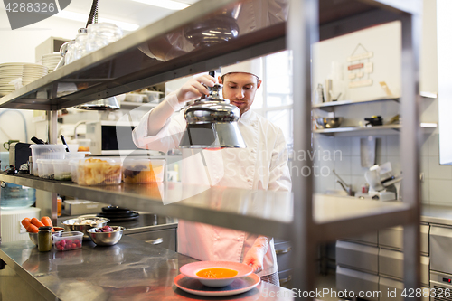 Image of male chef heating food with lamp at  kitchen