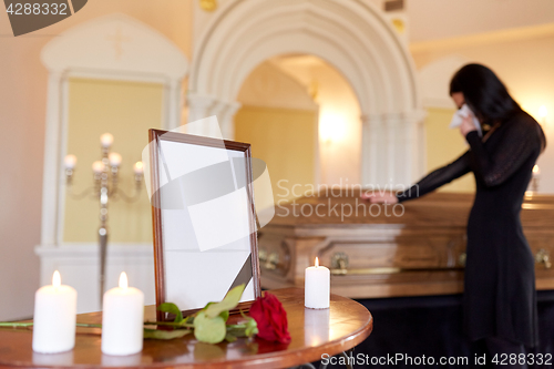 Image of photo frame and woman crying at coffin at funeral