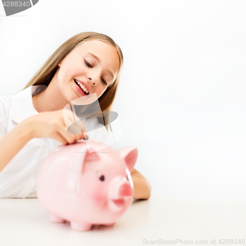 Image of happy smiling girl putting coin into piggy bank