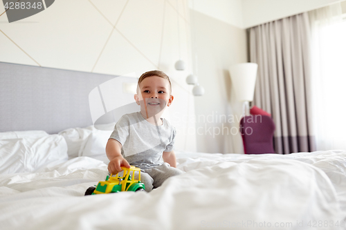 Image of happy little boy with toy car on home or hotel bed