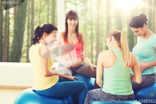 Image of happy pregnant women sitting on balls in gym