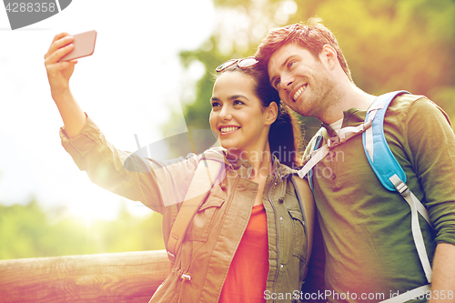 Image of couple with backpacks taking selfie by smartphone