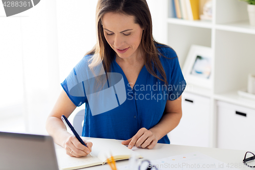 Image of happy woman writing to notebook at office