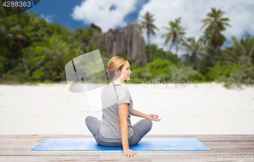 Image of woman doing yoga in twist pose on beach