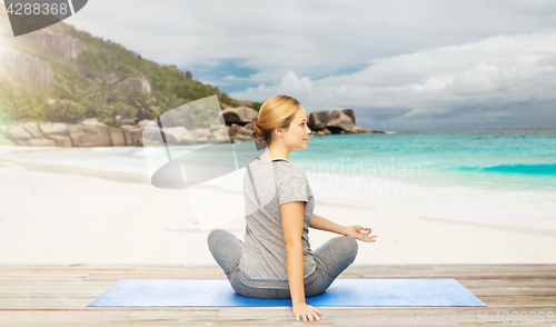 Image of woman doing yoga in twist pose on beach