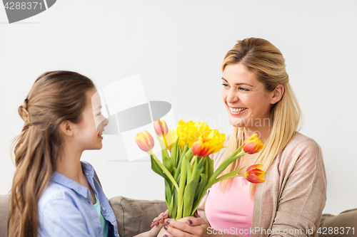 Image of happy girl giving flowers to mother at home