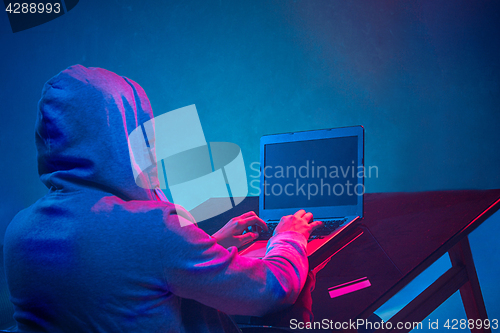 Image of Hooded computer hacker stealing information with laptop