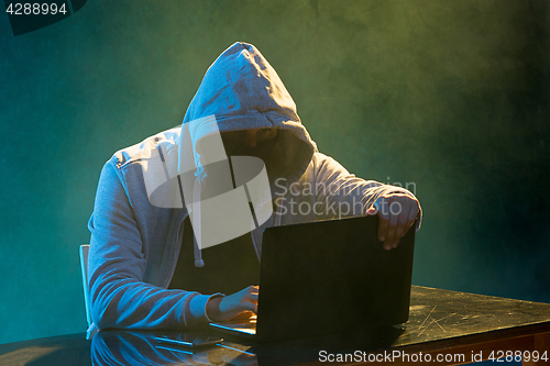 Image of Hooded computer hacker stealing information with laptop