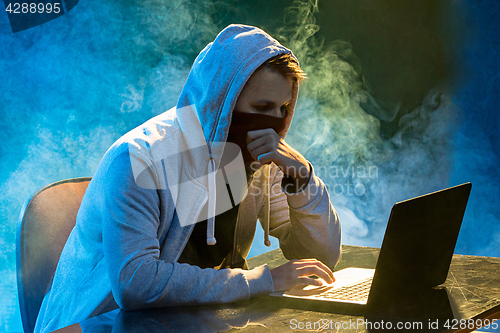 Image of Hooded computer hacker stealing information with laptop