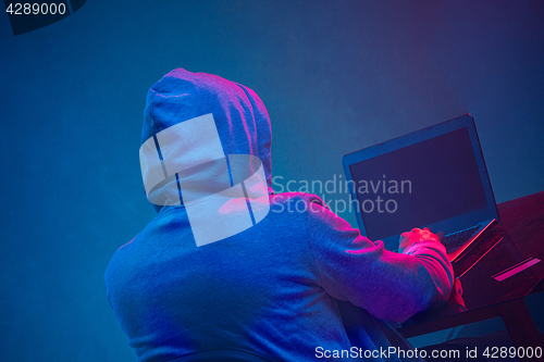 Image of Hooded computer hacker stealing information with laptop