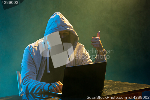 Image of Hooded computer hacker stealing information with laptop