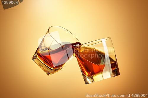 Image of Two whiskey glasses clinking together on brown