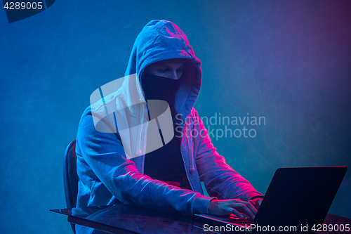 Image of Hooded computer hacker stealing information with laptop