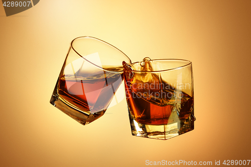 Image of Two whiskey glasses clinking together on brown