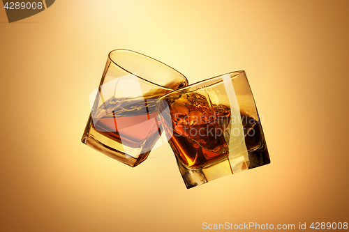 Image of Two whiskey glasses clinking together on brown