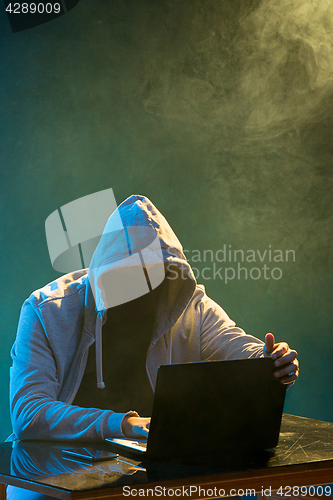 Image of Hooded computer hacker stealing information with laptop