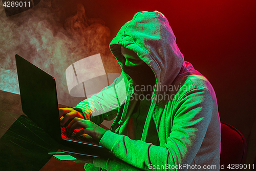 Image of Hooded computer hacker stealing information with laptop