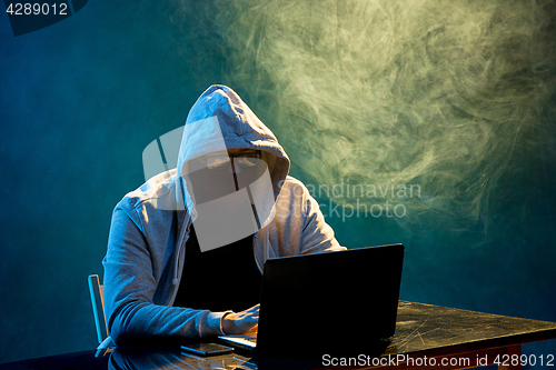 Image of Hooded computer hacker stealing information with laptop