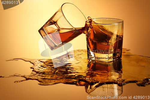 Image of Two whiskey glasses clinking together on brown