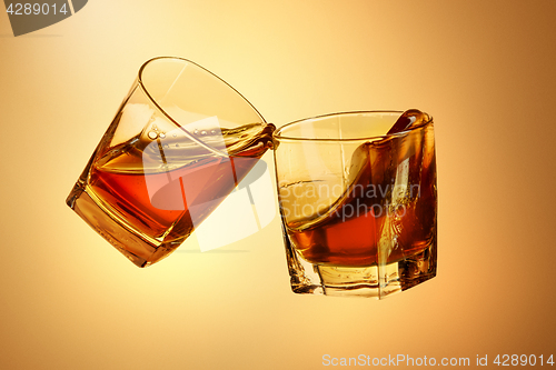 Image of Two whiskey glasses clinking together on brown