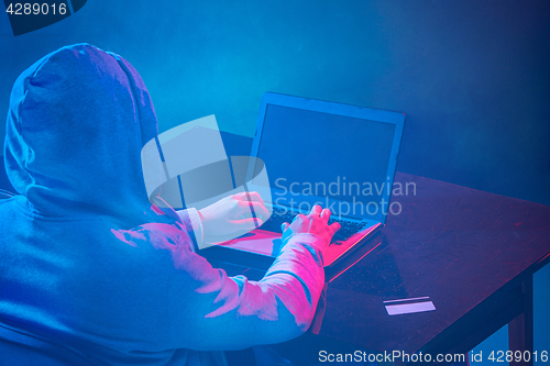 Image of Hooded computer hacker stealing information with laptop