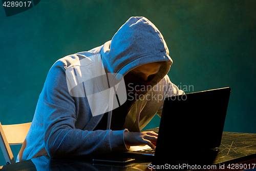 Image of Hooded computer hacker stealing information with laptop