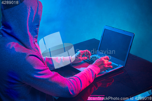 Image of Hooded computer hacker stealing information with laptop