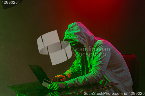 Image of Hooded computer hacker stealing information with laptop