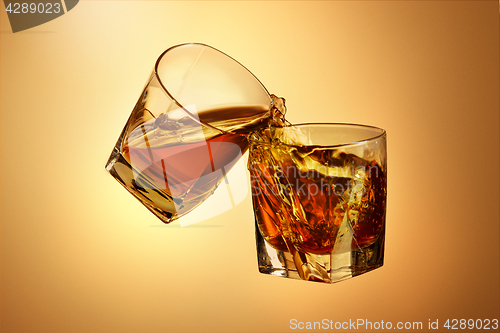 Image of Two whiskey glasses clinking together on brown