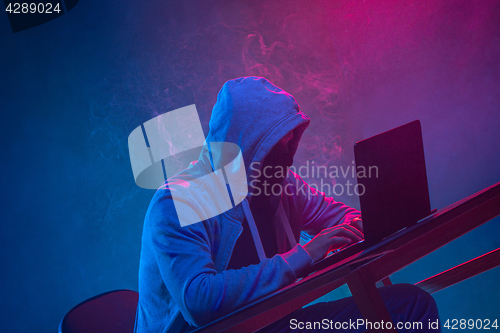 Image of Hooded computer hacker stealing information with laptop