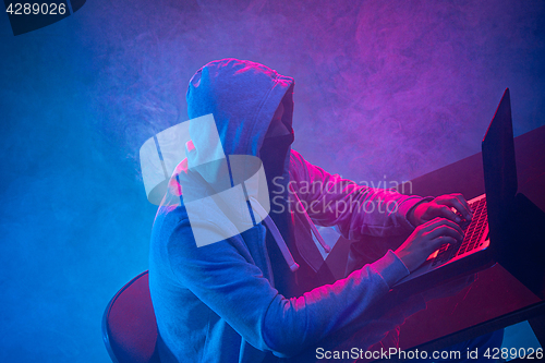 Image of Hooded computer hacker stealing information with laptop