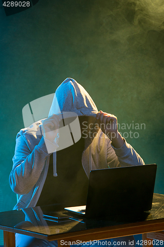 Image of Hooded computer hacker stealing information with laptop