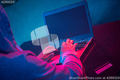 Image of Hooded computer hacker stealing information with laptop