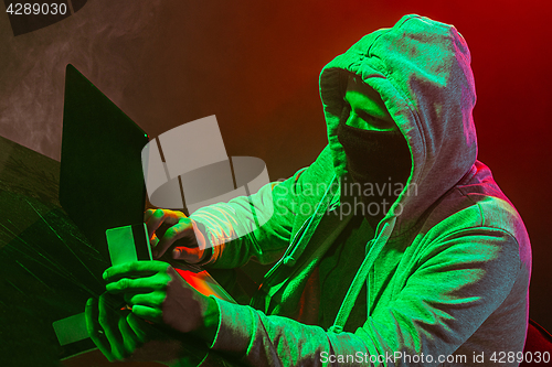 Image of Hooded computer hacker stealing information with laptop