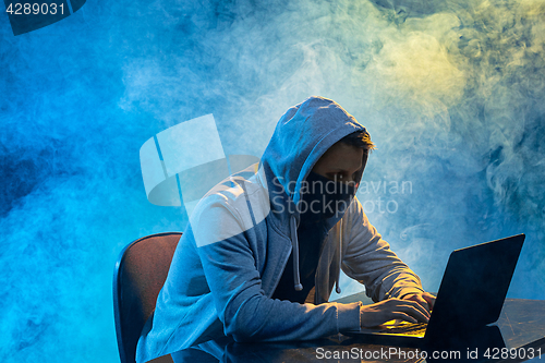 Image of Hooded computer hacker stealing information with laptop