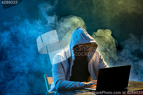 Image of Hooded computer hacker stealing information with laptop