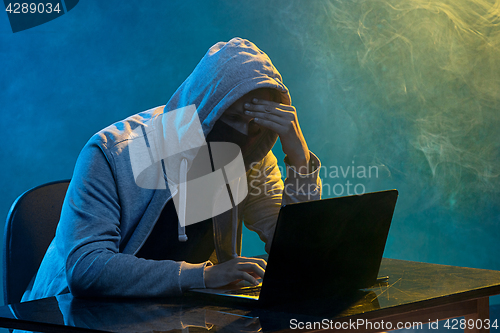 Image of Hooded computer hacker stealing information with laptop