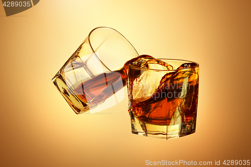 Image of Two whiskey glasses clinking together on brown