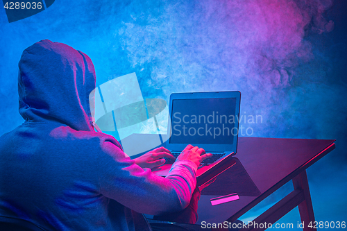 Image of Hooded computer hacker stealing information with laptop