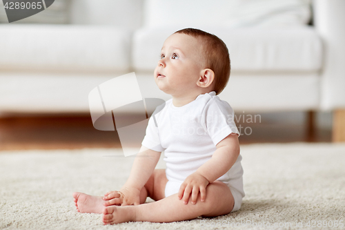 Image of happy baby boy or girl sitting on floor at home