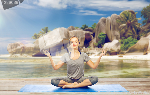 Image of woman doing yoga meditation in lotus pose on beach