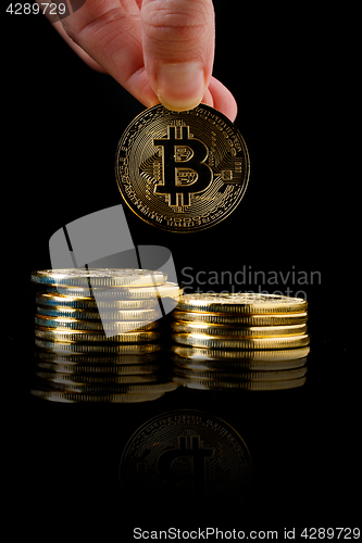 Image of hand pouring bitcoin from row on black background, conceptual