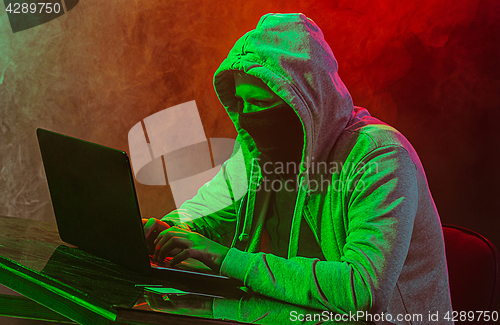 Image of Hooded computer hacker stealing information with laptop