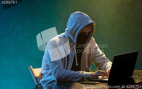 Image of Hooded computer hacker stealing information with laptop