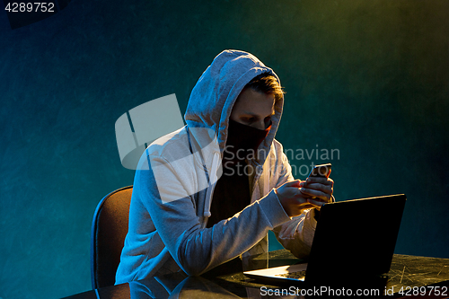 Image of Hooded computer hacker stealing information with laptop